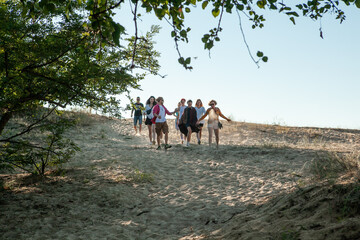 a company of men and women walking along the sandy beach in the summer