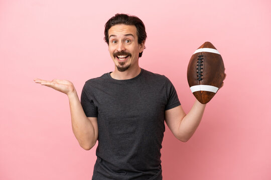 Young caucasian man playing rugby isolated on pink background with shocked facial expression