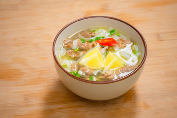 Spicy pho soup bowl with beef meat, lemon slice and chilli peppers on wooden table. Home delivery