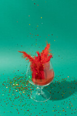 Glass with sequins and red feathers on a green background