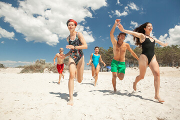 a group of friends consisting of men and women running on the beach in the sea