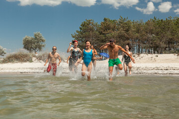 a group of friends consisting of men and women running on the beach in the sea