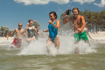 a group of friends consisting of men and women running on the beach in the sea