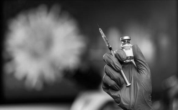 Hand wearing blue medical gloves hoding bottle of Covid-19 vaccine and syringe ready to give injection with virus image blur in background