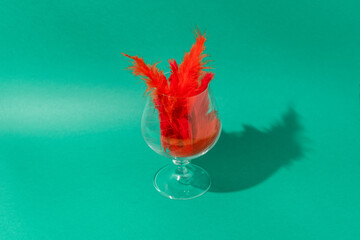Glass with red feathers on a green background