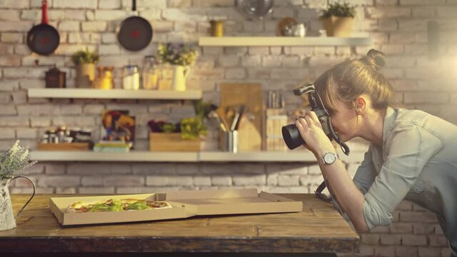 Woman photographing take away pizza on the kitchen table at home.