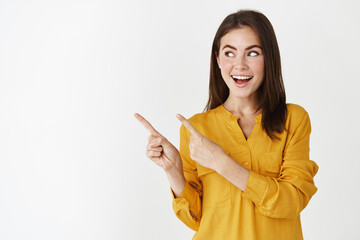 Image of smiling young woman showing her choice, pointing fingers and looking left with confident expression, demonstrating logo, standing over white background - 442893030
