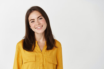 Beauty and lifestyle concept. Young brunette woman smiling and looking at camera, showing happy face and confidence, standing on white background