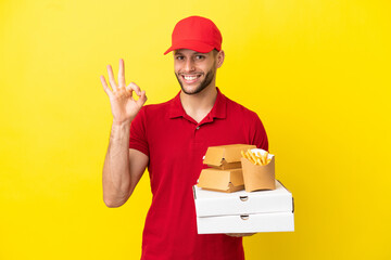 pizza delivery man picking up pizza boxes and burgers over isolated background showing ok sign with...