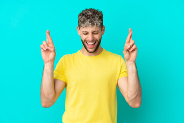 Young handsome caucasian man isolated on blue background with fingers crossing
