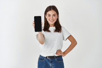 Young beauty woman holding blank screen mobile phone and smiling, showing smartphone display,...