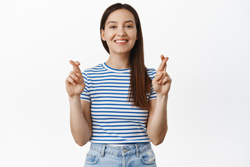 Smiling optimistic woman cross fingers for good luck, makes wish, self-assured in positive result, anticipating good news, looking hopeful and happy at camera, faithful, white background