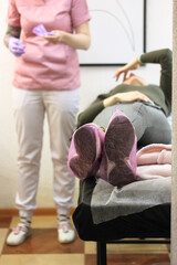 A patient wearing pink shoe covers on examination couch in diagnostic cabinet.