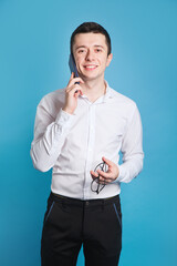 Portrait of a young business man wearing white shirt using mobile phone on blue background