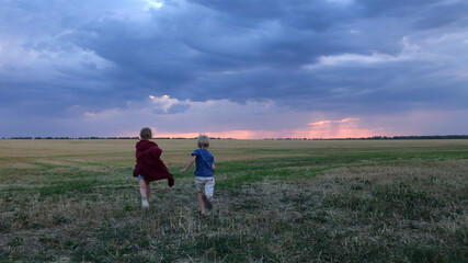 Two children run across a field against the background of clouds at sunset.A boy and a girl in a field against the background of storm clouds