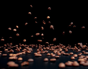Roasted coffee beans on a black background in the process of falling