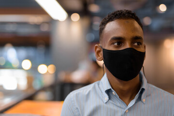 Portrait of handsome black African businessman inside shopping mall wearing face mask while thinking