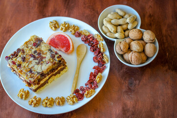 Piece of tasty chocolate-nut cake on a white plate. Walnuts and wooden spoon stand nearby