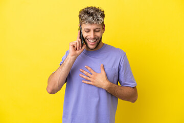 Young caucasian man using mobile phone isolated on yellow background smiling a lot