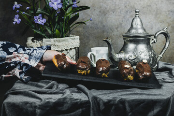 closeup woman wearing beautiful blue dress holding a plate french dessert eclairs with custard and chocolate icing and decorated with hazelnuts