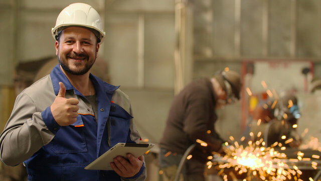 Engineer looking at camera smiling and showing thumb up at metallurgy plant