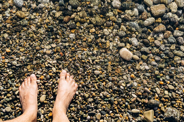 Legs of a man on the shore of a stone beach of the sea. Space for copying text