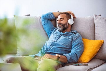 Relaxed middle-aged man listening to music with headphones. Joyful mature male enjoying melody from...