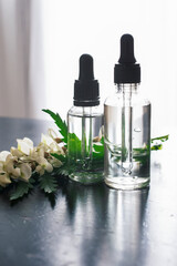 Transparent bottles of cosmetics with fresh flowers are on the table. Cosmetic oil