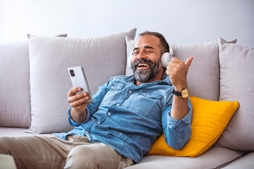 Time to relax. Handsome middle-aged bearded man in wireless headphones listening to music online on smartphone, copy space, closeup. Happy man in headset watching videos on mobile phone