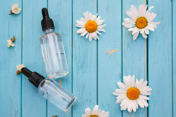 Jars of cosmetics lie on a blue wooden background with fresh flowers and leaves. Natural cosmetics