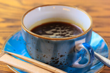 Blue ceramic cup on a saucer with black coffee on a brown wooden background.