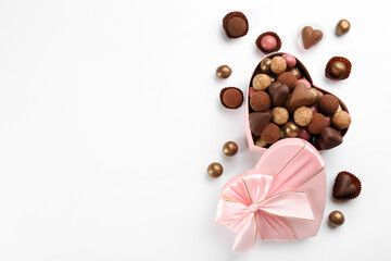 Different delicious chocolate candies in heart shaped box on white background, flat lay. Space for text