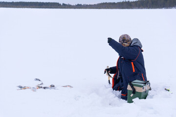 Fototapeta na wymiar ice fishing. fisherman fishing on a winter lake against a background of forest and blue sky.