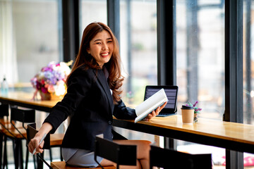 Portrait of businesswoman wearing black jacket, she is working on the computer at coffee shop.