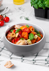 Salad with baked vegetables, croutons, olives, capers, cherry tomatoes, basil and olive oil served in the gray bowl. Mediterranean meal