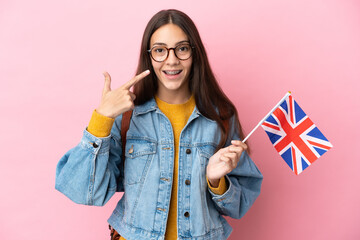 Young French girl holding an United Kingdom flag isolated on pink background giving a thumbs up gesture