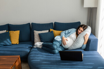 Smiling pregnant woman watching movie on laptop