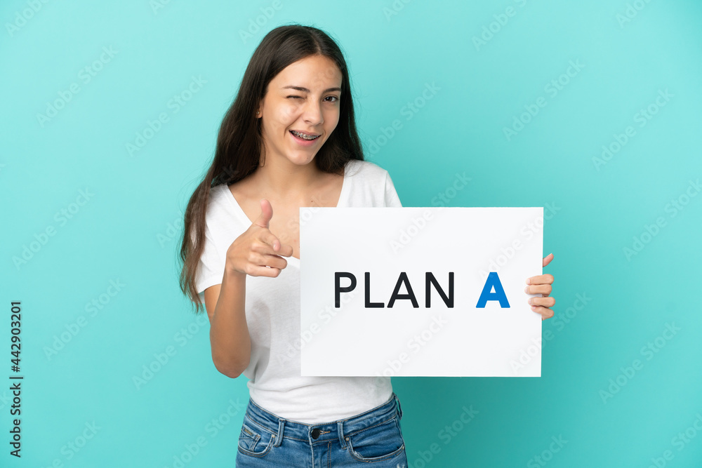 Wall mural young french woman isolated on blue background holding a placard with the message plan a and pointin