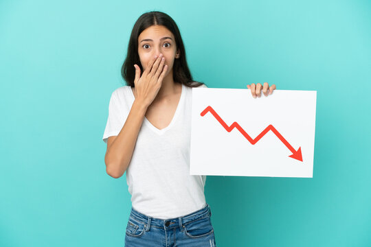 Young French woman isolated on blue background holding a sign with a decreasing statistics arrow symbol with surprised expression