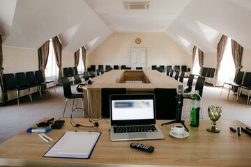 Front view of a wood table with equipment for meeting in empty conference room. Chairs and conference table on the background