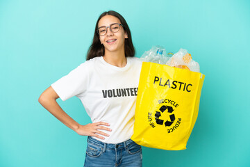 Young French girl holding a bag full of plastic bottles to recycle posing with arms at hip and smiling