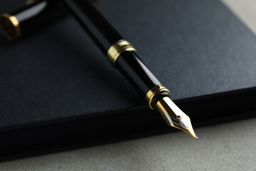 Beautiful fountain pen with ornate nib and black notebook on grey table, closeup