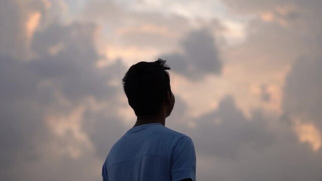 Portrait of an Indian kid happily looking at the orange sky with clouds during the sunset. Hopeful kid looking at the sky and smiling