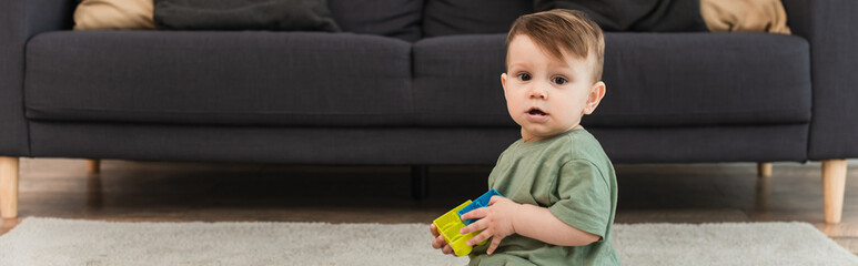 Toddler kid with building blocks looking at camera at home, banner