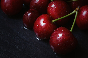 Cherry tree macro black background top view. Ripe juicy cherry berries in drops of water are lying on the table. The concept of freshness, proper nutrition, vitamins. Low key, close-up. Copy space