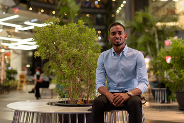 Portrait of handsome black African businessman sitting outdoors in city at night while smiling