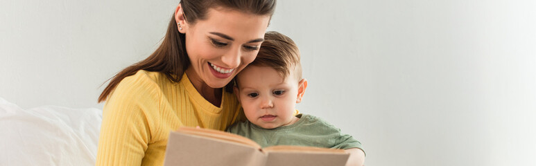 Young mother and child reading book near pillow at home, banner