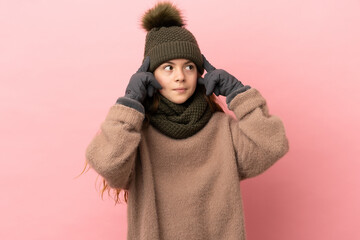 Little girl with winter hat isolated on pink background having doubts and thinking