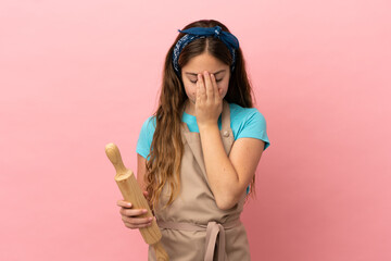 Little caucasian girl holding a rolling pin isolated on pink background with tired and sick expression