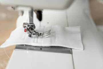 Sewing machine with with a white cloth on a wooden table.